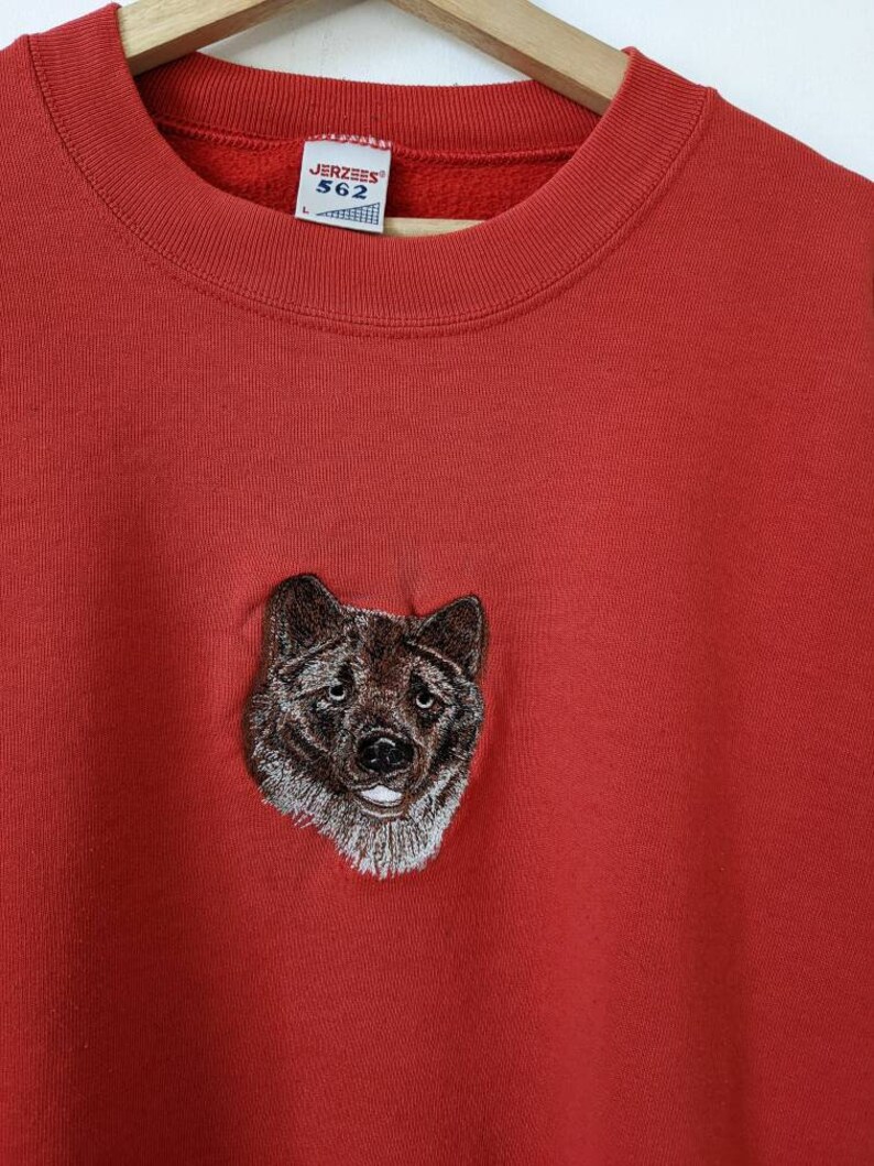 May include: Red sweatshirt with an embroidered wolf head on the front. The sweatshirt has a Jerzees tag with the size L and the number 562.