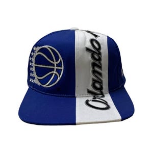 Op de afbeelding: Een blauwe en witte baseballpet met een basketbal en "Orlando" erop.