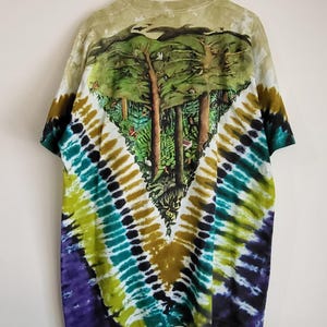 Puede incluir: Una camiseta te&ntilde;ida con un dise&ntilde;o de bosque en la espalda. La camiseta presenta un patr&oacute;n te&ntilde;ido en forma de V en tonos morado, verde, amarillo y marr&oacute;n. La escena del bosque representa &aacute;rboles y follaje.