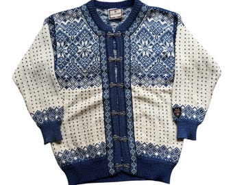 May include: Cream and navy blue cardigan sweater with a snowflake pattern. The sweater has a button-up front with silver-toned clasps, navy blue cuffs, and a navy blue collar. The sweater has a tag on the collar.