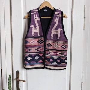 May include: A purple, pink, blue and black knitted waistcoat with a geometric pattern and two llama figures. The waistcoat has a button closure.