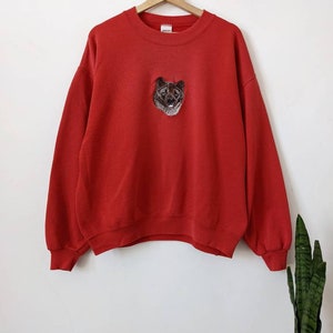 May include: Red sweatshirt with a black and white embroidered dog on the front.