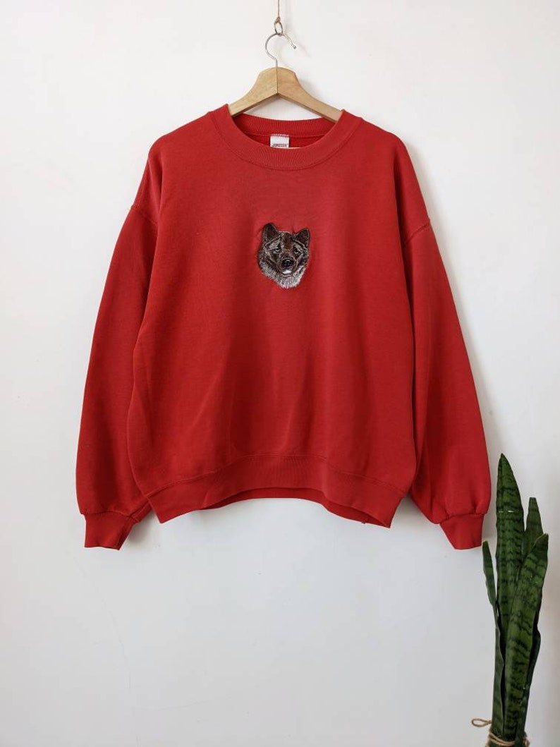May include: Red sweatshirt with a black and white embroidered dog on the front.