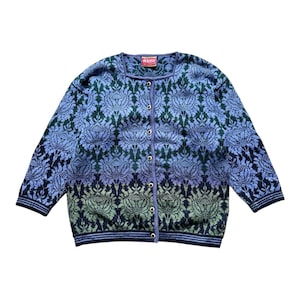 Pode incluir: Cardigã com botões com um padrão floral em tons de azul, verde e roxo. O suéter tem um decote quadrado e mangas compridas. Uma pequena etiqueta é visível no topo. O suéter é feito de um material de malha macia.