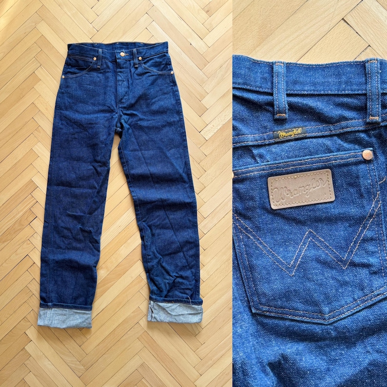 Op de afbeelding: Donkerblauwe denim jeans met een rechte pijp en een knoopsluiting. De jeans hebben een klassiek vijf-zakken ontwerp en een leren patch op de achterzak met het "Wrangler" logo. De manchetten zijn opgerold.