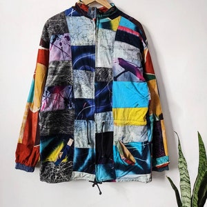 Pode incluir: Uma jaqueta colorida de patchwork com fecho de correr e cordão de ajuste na parte inferior. A jaqueta é feita de diferentes tecidos com vários padrões e cores, incluindo azul, vermelho, amarelo e preto.
