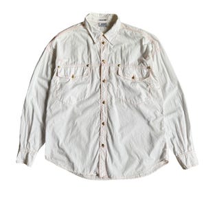 May include: A long-sleeve button-down shirt in off-white fabric with contrasting orange stitching. The shirt features two chest pockets with gold-toned metal buttons, a standard collar, and a Gianni Versace label at the inner neckline.