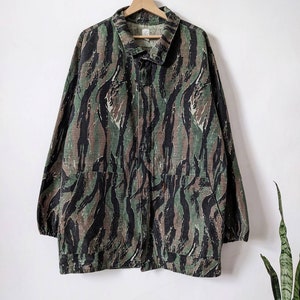 May include: A green, black and brown camouflage jacket with a button-up front and long sleeves.