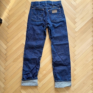 Op de afbeelding: Donkerblauwe spijkerbroek met een klassiek vijf-zakken ontwerp. De jeans heeft een rechte pijp, opgevouwen manchetten en een bruine leren patch op de rug. De stiksels zijn in contrasterend goud.
