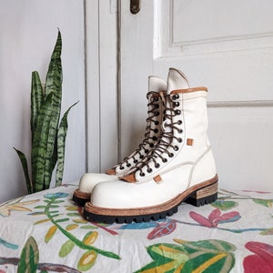 May include: White leather lace-up boots with a thick brown sole. The boots are sitting on a floral patterned fabric.