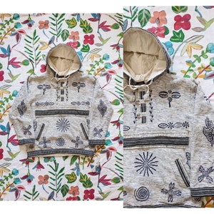 May include: A grey hooded sweatshirt with a black and white patterned design. The design features a variety of symbols, including a sun, a spiral, and a stylised eye. The sweatshirt has a drawstring hood and a kangaroo pocket.