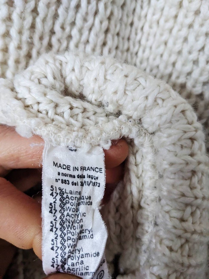 May include: A white knitted sweater label with the text "MADE IN FRANCE" and a list of materials and percentages, including "51% Laine", "47% Acrylique", "2% Polyamide", "47% Wool", "2% Acrylic", "51% Nylon", "47% Polyacryl", "2% Polamid", "47% Acry!", "51% Polyamide", "47% Lana", "Acrilic", "Poliamm".