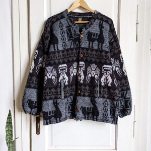 Könnte beinhalten: Ein schwarzer, grauer und weißer gemusterter Cardigan mit Knöpfen. Der Cardigan zeigt ein Design mit Lamas und geometrischen Mustern.
