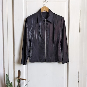 Puede incluir: Una chaqueta negra con cremallera y un brillo satinado. La chaqueta tiene cuello y mangas largas.