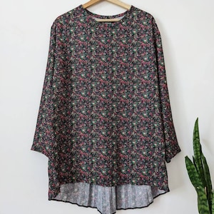 May include: A black long-sleeved tunic with a floral print in shades of pink, green, and white. The tunic has a rounded neckline and a slightly flared hem.