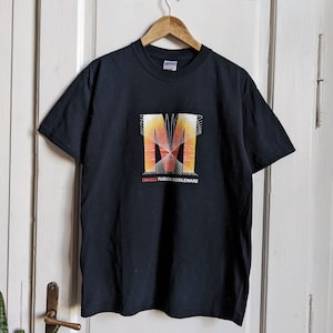 Könnte beinhalten: Schwarzes T-Shirt mit einem Grafikdruck eines stilisierten Buchstabens "M" in Orange, Gelb und Rot. Der Text "Oracle Fusion Middleware" ist unter dem Grafikdruck aufgedruckt.