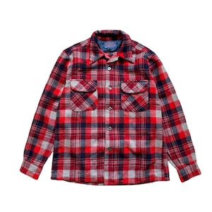 May include: A long-sleeved button-down shirt featuring a red, navy blue, and grey plaid pattern. The shirt includes a pointed collar, two chest pockets with buttoned flaps, and a front button closure. A Pendleton brand label is visible at the neck.