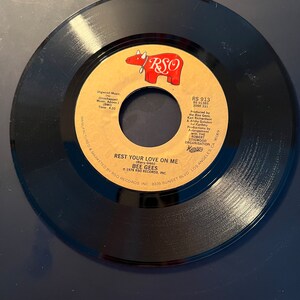 May include: A black vinyl record with a tan and red label. The label features the text "REST YOUR LOVE ON ME" by the Bee Gees, along with the RSO Records logo. The record is a 45 RPM single.