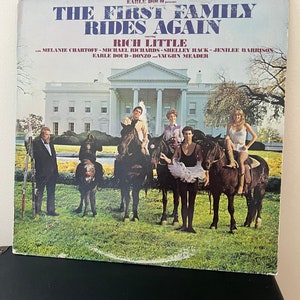 May include: Vintage vinyl record album cover for "The First Family Rides Again" starring Rich Little. The cover features a photo of people on horses in front of the White House. The album title and cast names are printed in blue.