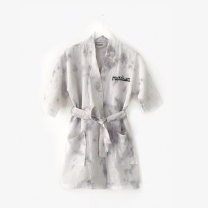 May include: A white waffle weave robe with a gray tie-dye pattern. The robe has a black embroidered name "madison" on the front.