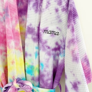May include: A purple, pink, yellow, and blue tie-dye waffle robe with a white background. The robe has a belt and the word "mama" embroidered on the front.