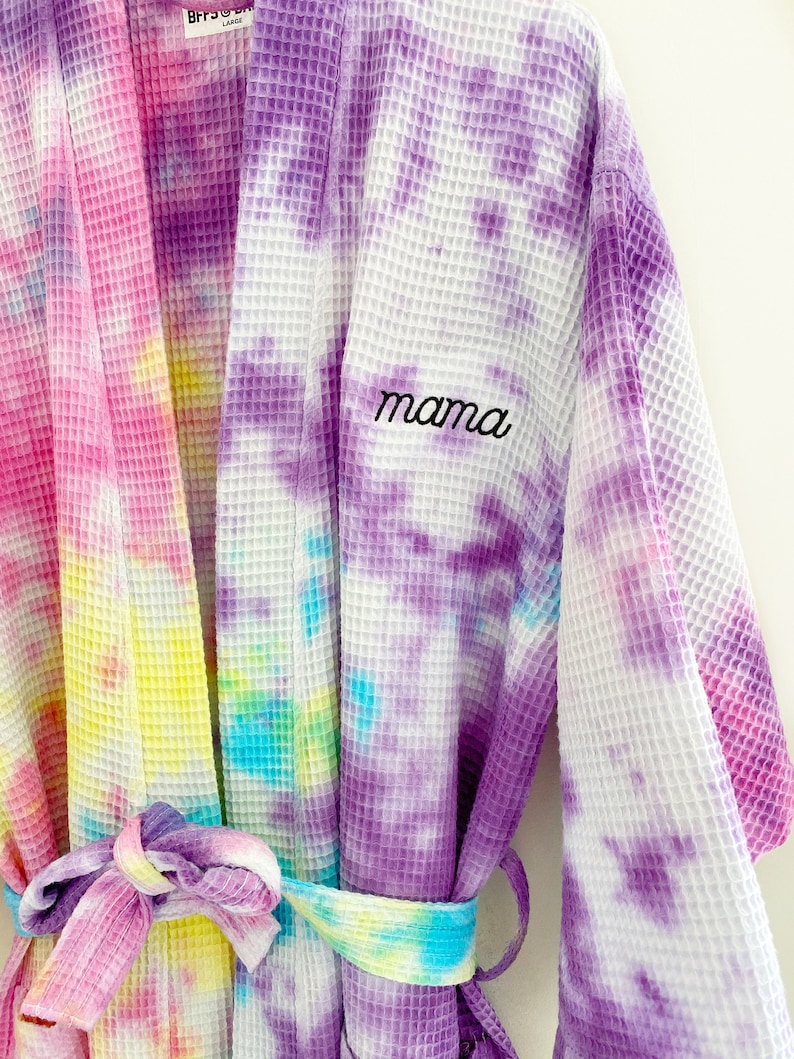 May include: A purple, pink, yellow, and blue tie-dye waffle robe with a white background. The robe has a belt and the word "mama" embroidered on the front.
