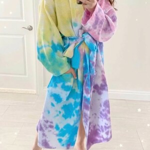 May include: A long, tie-dye robe with a blue, purple, yellow, and white pattern. The robe has a sash tie at the waist and long sleeves.