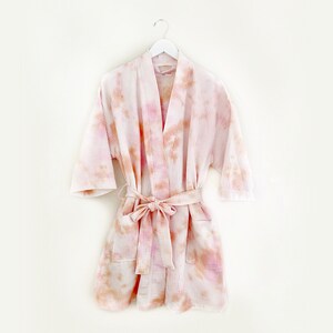 May include: A pink and orange tie-dye robe with a self-tie sash. The robe has a relaxed fit and is made of a soft, lightweight fabric.
