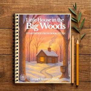 Peut inclure: Un livre à spirales intitulé "Little House in the Big Woods" avec une illustration de scène hivernale. La couverture présente une cabane, un chemin enneigé et des arbres dénudés. Deux crayons et une brindille de verdure reposent à côté du livre sur une surface en bois.