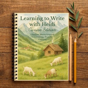 Peut inclure: Cahier à spirales intitulé "Learning to Write with Heidi Cursive Edition" avec une illustration de paysage de montagne, des chèvres et une cabane. Deux crayons et de la verdure sur une surface en bois.