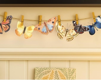 May include: A collection of colorful butterfly decorations clipped to a string with wooden clothespins. The butterflies feature various patterns and shades of orange, yellow, blue, and brown. The background is a neutral cream color.