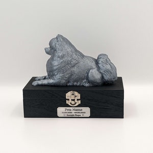 May include: A silver-coloured figurine of a Pomeranian dog lying down on top of a black wooden box with a silver latch. The box has a silver plaque with the text "Pets Name 11.09.2010 - 09.08.2023  ♥ Example Plaque ♥".