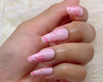May include: Pink and gold marble design press-on nails. The nails are long and have a coffin shape.