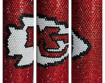 May include: A red, bedazzled tumbler featuring the Kansas City Chiefs logo. The logo is composed of white, black, and red elements. The tumbler is covered in small, sparkling red rhinestones, creating a shimmering effect.