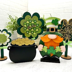 May include: A set of five St. Patrick's Day decorations featuring a green leprechaun holding a pot of gold, a green shamrock, a pot of gold, and two shamrock flowers. The decorations are made of wood and have a festive, whimsical design.