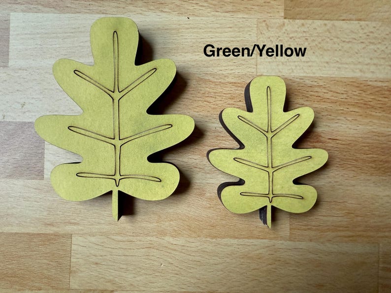 May include: Two flat, leaf-shaped cutouts in a light green-yellow color, featuring dark brown edges and engraved vein details. The larger leaf is on the left and the smaller leaf is on the right. The text "Green/Yellow" is printed above the smaller leaf.
