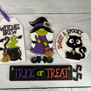 May include: Four Halloween-themed wooden signs with purple, green, black, and white paint. The signs read "Witches Brew", "Sweet & Spooky", "Trick or Treat", and feature a witch, a black cat, and a cauldron.