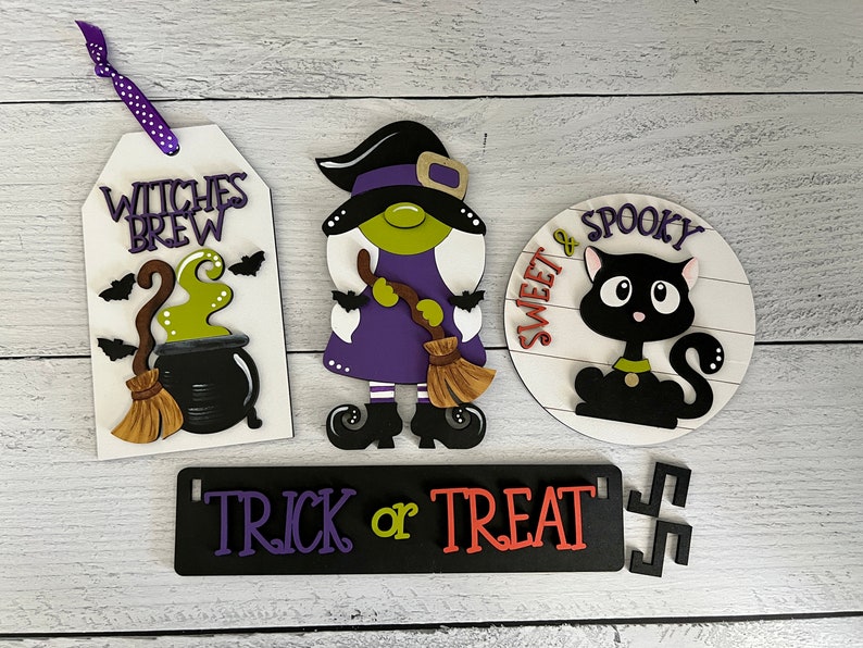 May include: Four Halloween-themed wooden signs with purple, green, black, and white paint. The signs read "Witches Brew", "Sweet & Spooky", "Trick or Treat", and feature a witch, a black cat, and a cauldron.