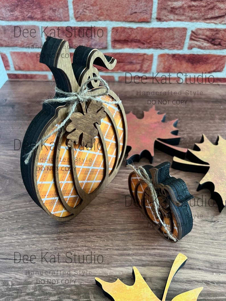 May include: Two layered wooden pumpkin decorations featuring an orange and white plaid pattern, black edges, and a jute twine bow with a small wooden leaf accent. Two separate wooden maple leaf cutouts in orange and brown tones are also included.
