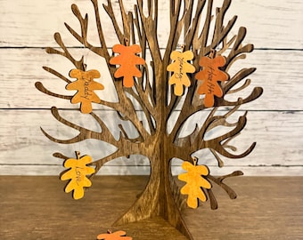 May include: A dark brown wooden tree sculpture with multiple branches, featuring several hanging orange and yellow leaf-shaped ornaments. Some leaves are inscribed with the words Daddy, Family, Heath, and Love in black script.