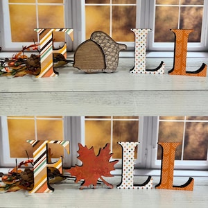 May include: A set of decorative wooden letters spelling FALL, featuring an F with diagonal stripes, an L with polka dots, and an L with a chevron pattern. The A is replaced by either a wooden acorn or a red maple leaf cutout.