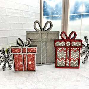 May include: Three wooden Christmas gift boxes with glitter accents. The boxes are decorated with different patterns in red and gray. Two snowflakes are also included.