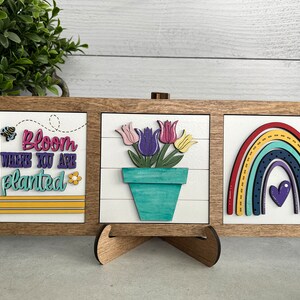 K&ouml;nnte beinhalten: Drei Holzschildchen mit einem Bauernhof-Thema. Das erste Schild sagt "Bloom where you are planted" mit einer Biene und einer Blume. Das zweite Schild hat einen Blumentopf mit bunten Tulpen. Das dritte Schild hat einen Regenbogen mit einem Herzen in der Mitte.