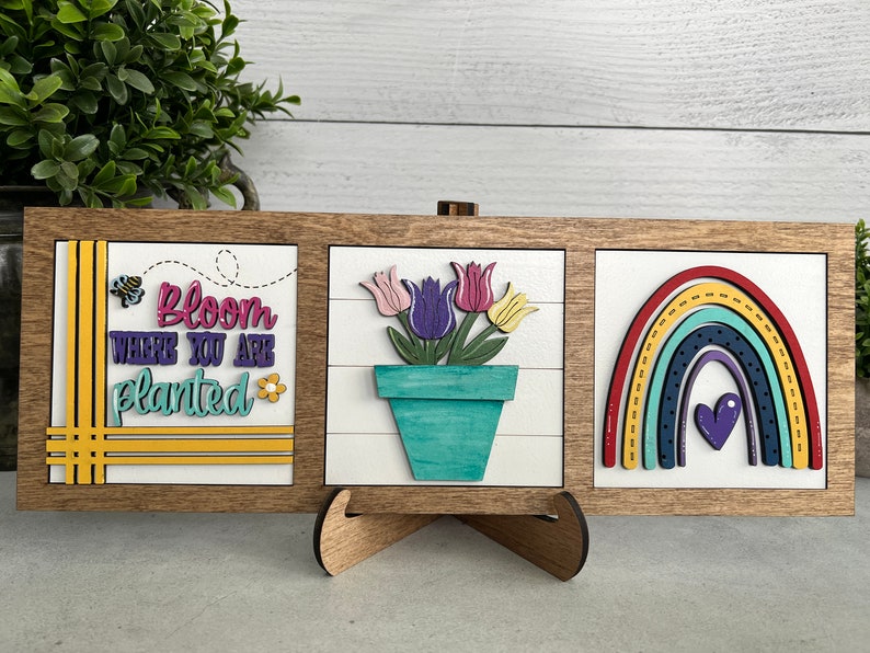 K&ouml;nnte beinhalten: Drei Holzschildchen mit einem Bauernhof-Thema. Das erste Schild sagt "Bloom where you are planted" mit einer Biene und einer Blume. Das zweite Schild hat einen Blumentopf mit bunten Tulpen. Das dritte Schild hat einen Regenbogen mit einem Herzen in der Mitte.