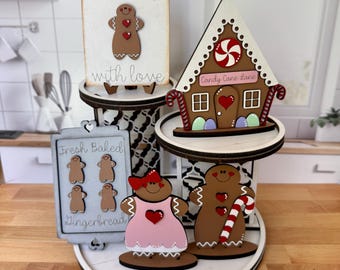 May include: A tiered wooden display featuring gingerbread-themed decorations. Includes a cutting board with a gingerbread man, a gingerbread house, and gingerbread people. The display is decorated with red and white accents and the text "Baked with love", "Candy Cane Lane", and "Gingerbread".