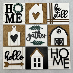 May include: Nine wooden signs with various farmhouse-themed designs. The signs feature black and white lettering, green leaves, and a brown wood grain background. The signs read "HOME", "gather", "be still", "hello", "HOME", and a house, a cutting board, and a barn.