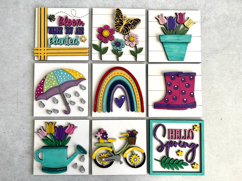 K&ouml;nnte beinhalten: Neun Holzschilder mit Fr&uuml;hlingsmotiven. Die Schilder zeigen einen Regenbogen, einen Schmetterling, eine Gie&szlig;kanne, ein Fahrrad, Gummistiefel, einen Regenschirm, eine Topfpflanze und den Text "Bloom where you are planted" und "Hello Spring".