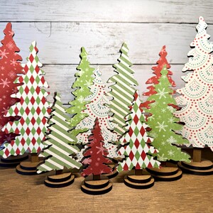 May include: A collection of ten flat, cutout wooden Christmas tree decorations of varying heights. Each tree features a unique pattern, including red with white snowflakes, green and red diamonds, green stripes, and white with red scalloped designs.