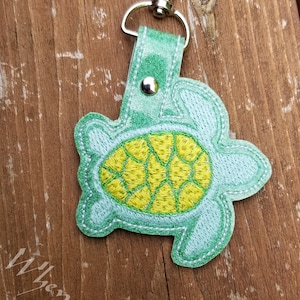 May include: A light blue and yellow embroidered turtle keychain with a silver clasp.