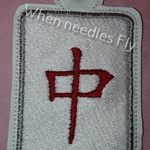 May include: A white fabric key tag with a gray border and a red Chinese character embroidered on it. The text "When Needles Fly" is visible in the background.